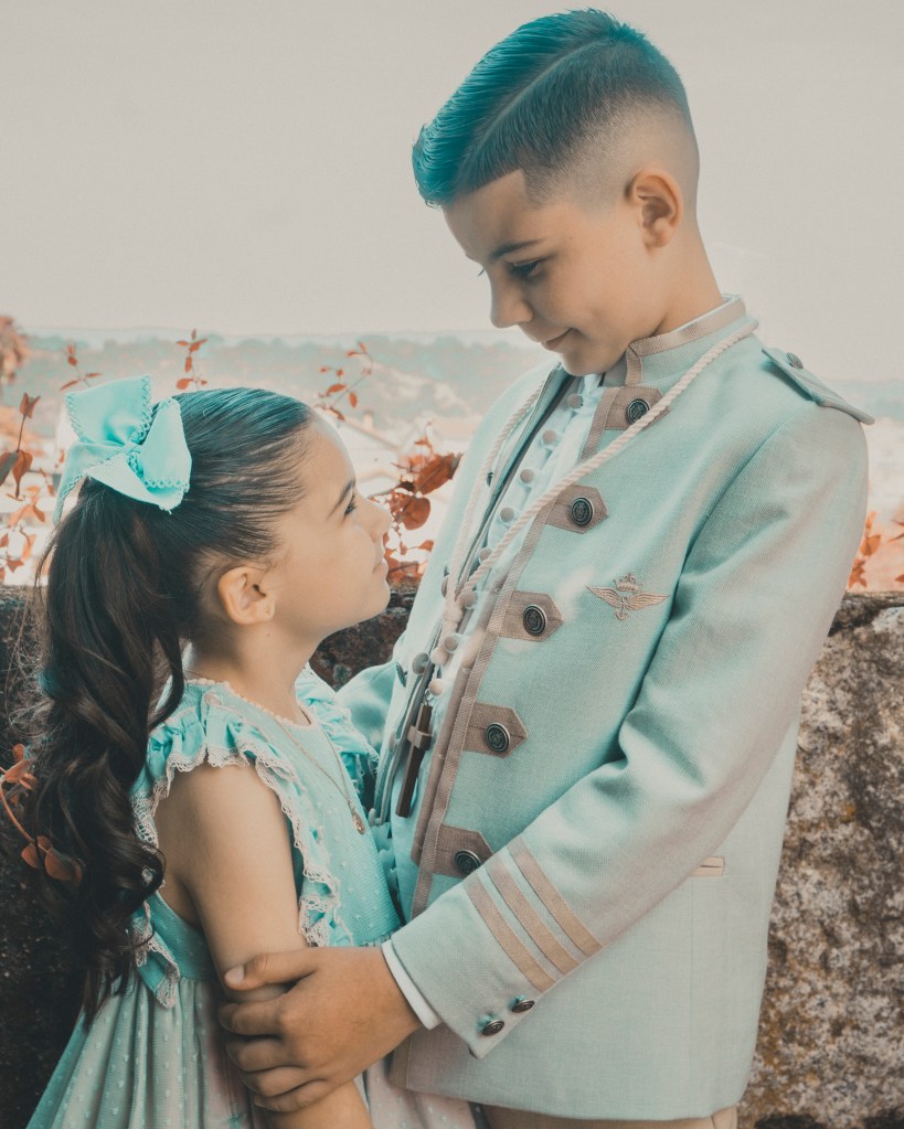 Fotografía de hermanos el día de su Primera Comunión con traje azul claro, sonriendo al aire libre en Ourense